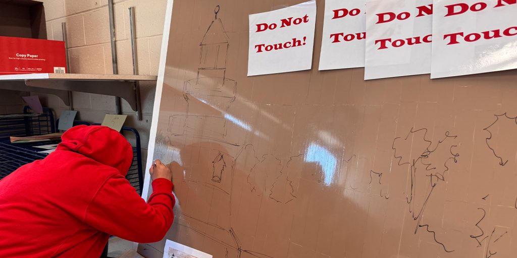 A student drawing on a board. The board is lined Pro Tapes white Pro Artist Tape.