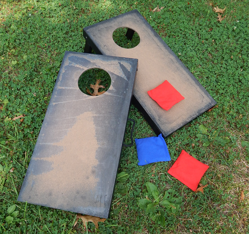 Two unfinished cornhole boards Becky found at a garage sale. She sanded them to down to prepare them for spray painting, but...